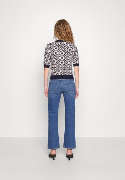 Patterned knit top with short sleeves, featuring a geometric design in navy and cream. Paired with blue flared jeans and black heels.