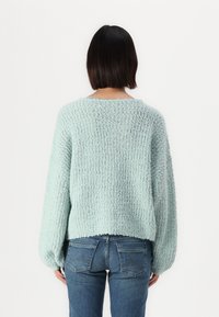 Pull en maille bleu clair, à la coupe ample, avec des manches larges et un col rond. Associé à un jean bleu foncé.