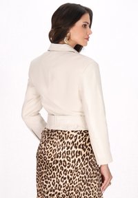 Giacca in pelle crema con un design aderente, vita regolabile con cintura e maniche lunghe, abbinata a una gonna con stampa leopardata. Textura liscia, hardware minimale.