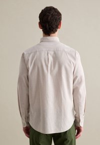 Camisa de manga larga beige claro con finas rayas verticales, cuello abotonado, pliegues en la parte trasera y mangas con puños, combinada con pantalones verdes.