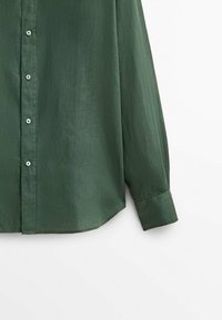 Tummanvihreä nappipaita, valmistettu sileästä kankaasta. Siinä on pitkät hihat, pyöristetty helma ja vaaleanvihreät napit edessä.