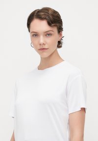 T-shirt bianco a maniche corte realizzato in tessuto morbido, con una vestibilità comoda e scollo rotondo, presentato su uno sfondo bianco uniforme.