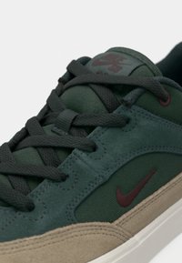 Green and gray Nike sneakers with a suede and textile upper, featuring dark gray laces and a maroon logo on the side. Soft sole detail visible.
