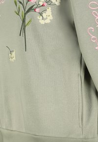 Hellgrüner Pullover mit floraler Stickerei in Weiß und Rosa. Verfügt über eine Vorderseite mit Tasche sowie einen gerippten Saum und Bündchen. Weiche Textur.