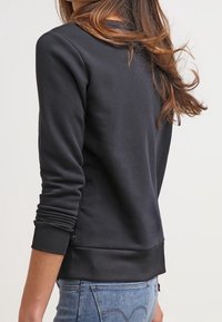 Mörkgrå sweatshirt med långa ärmar, muddade fållar och en knappdetalj längst ner. Mjuk, slät textur och figurnära design.