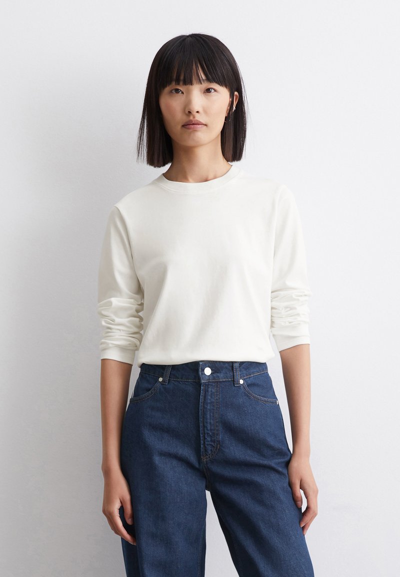 Hvid langærmet bomulds T-shirt med rund halsudskæring, parret med højtsiddende mørkeblå denimjeans med en frontknap og lommer.