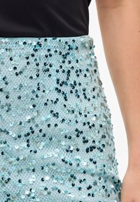 Jasnoniebieska spódnica z cekinami, charakteryzująca się teksturowaną, błyszczącą powierzchnią oraz dopasowanym krojem. Wzory okrągłych cekinów różnią się wielkością i kolorem.