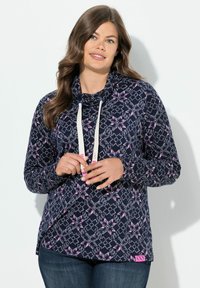 Marinblå huvtröja med rosa och vita geometriska mönster. Har en hög krage, snoddar och en etikett nederst. Tillverkad av ett mjukt material.