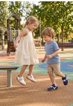 Dos niños pequeños jugando alegremente en un colorido parque infantil al aire libre con árboles y bancos al fondo.