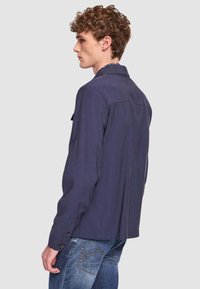 Camicia casual blu navy con colletto button-down, maniche lunghe e due tasche sul petto, caratterizzata da una texture liscia e una vestibilità strutturata.