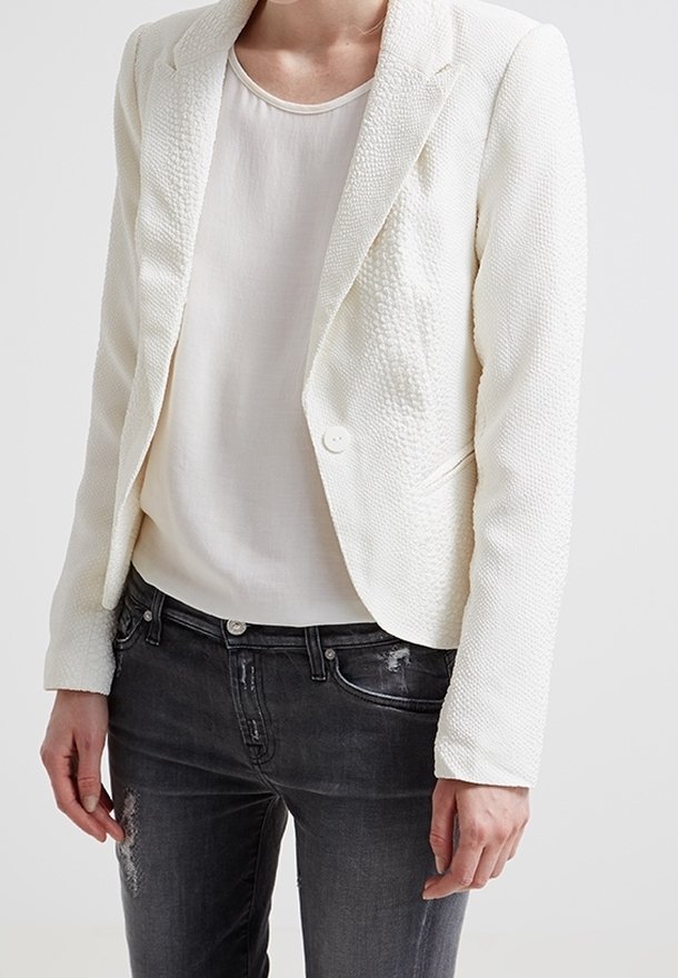 Blazer blanc texturé à fermeture par un bouton unique, porté sur une chemise claire et associé à un jean noir déchiré.