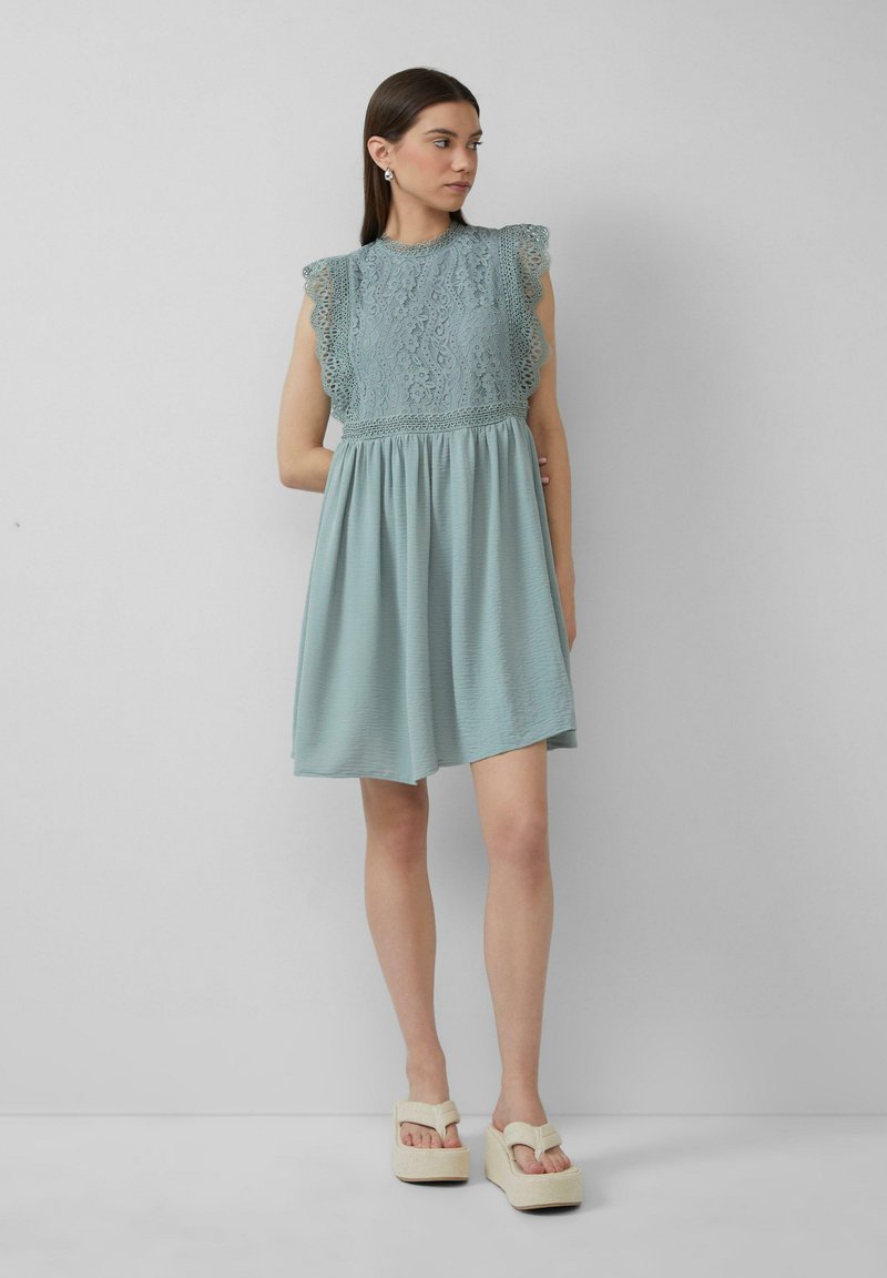 Robe bleu clair avec un haut en dentelle, des manches volantes et une jupe fluide. Assortie avec des sandales à plateforme beige présentant un design à larges lanières.