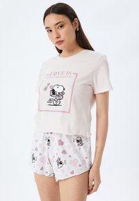 T-shirt courte rose clair avec un graphique de chien cartoon noir, associé à un short blanc avec des motifs de coeurs roses et des éléments de dessin animé.