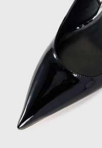 Scarpa con punta a punta in pelle verniciata nera, con finitura lucida e interno liscio. Presenta una silhouette elegante e senza hardware visibile.