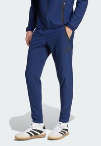 Marineblaue Sporthosen mit schmalem Schnitt, ausgestattet mit Reißverschlusstaschen, elastischem Bund und schwarzen Akzenten. Kombiniert mit schwarzen und weißen Sneakers.