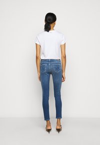 Smala blå jeans med bakfickor, tillsammans med en enkel vit T-shirt. Jeanserna har en medelblå tvätt och en slät textur.