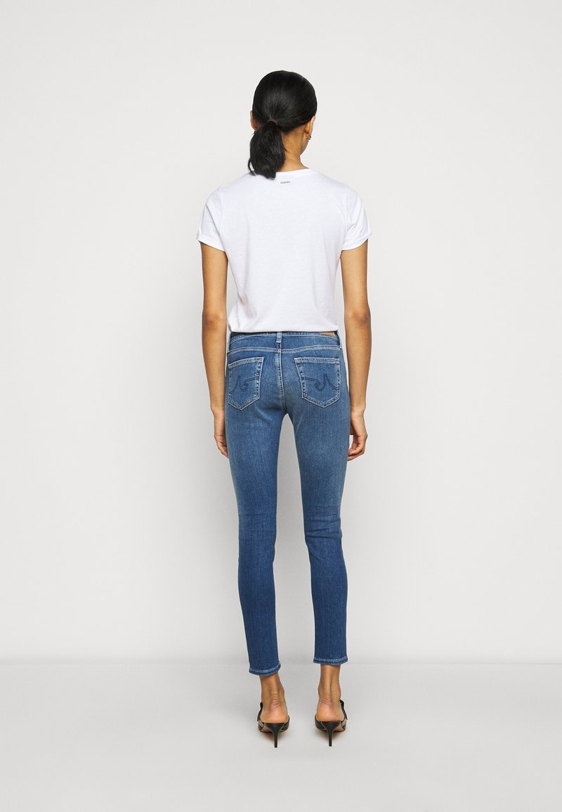 Smala blå jeans med bakfickor, tillsammans med en enkel vit T-shirt. Jeanserna har en medelblå tvätt och en slät textur.