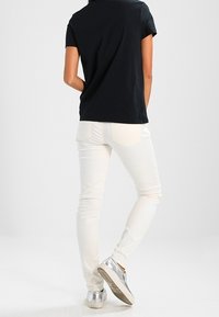 Černé tričko s krátkým rukávem, bílé slim-fit kalhoty a stříbrné slip-on boty. Hladké tkaniny, jednoduchý design, žádné vzory či ozdoby.