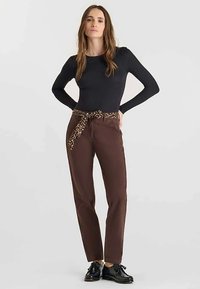 Bruine broek met een riem met luipaardprint, zwart topje met lange mouwen en zwarte schoenen. De stof lijkt glad en het ontwerp is nauwsluitend.