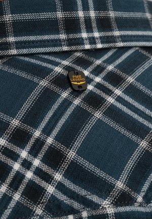 Tummansininen flanellipaita, jossa on valkoista ja harmaata ruutukuviota. Sisältää mustan tarran, jossa on keltainen teksti "PME LEGEND." Pehmeä kangas, taitettu muoto.