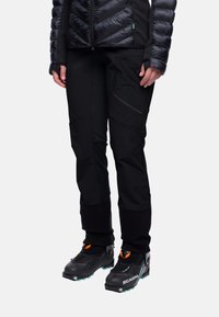 Zwarte soft-shell broeken met taps toelopende benen, ritszakken, versterkte knieën en gecombineerd met zwart en oranje bergschoenen.