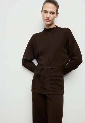 Top de punto marrón con un cuello alto, hombros caídos y cintura atada. Combinado con pantalones de pierna ancha marrones a juego. Textura suave.