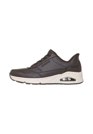 Zapatilla atlética marrón con parte superior de cuero texturizado, entresuela gris claro, detalles de amortiguación de aire y suela exterior de goma negra en contraste.