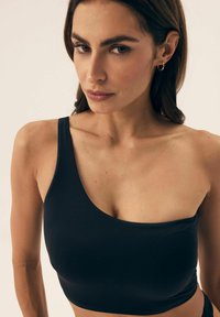 Czarny top na jedno ramię wykonany z gładkiego materiału, charakteryzujący się skróconą długością oraz okrągłym dekoltem i minimalnymi detalami szewnymi.