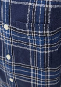 Modrá, biela a čierna kockovaná látka s predným vreckom a bielymi gombíkmi na košeli na gombíky.