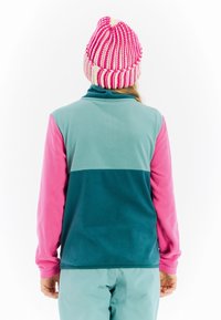 Fleecejack met een teal lichaam en roze mouwen, hoge kraag, en een gebreide beanie met een textuur in roze en witte strepen.