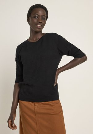 Schwarzer, strukturierter Strickpullover mit Dreiviertelärmeln, rundem Ausschnitt und enganliegenden Bündchen, kombiniert mit einem braunen Rock.