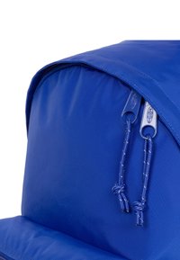 Modrý nylonový batoh s zaobleným tvarem, vybavený dvojitými zipy a akcenty na šňůrce. Hladký povrch s vyztuženými švy.