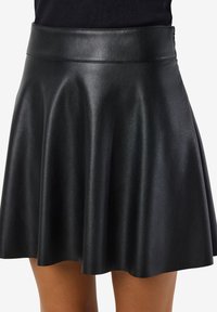 Jupe patineuse en simili cuir noir avec une texture lisse, une taille ajustée et un bas évasé, créant une silhouette fluide.