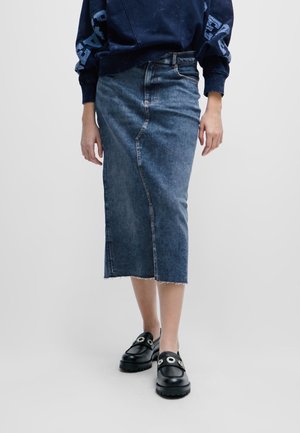 Denim midi rok in donkerblauw met een rechte pasvorm, subtiele stiksels en een rafelige zoom. Gecombineerd met zwarte platform schoenen met oogjes.