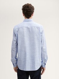 Chemise à manches longues bleu clair avec un aspect tissé et texturé. Dotée d'un col pointu et de poignets boutonnés. L'ourlet est arrondi à l'arrière.