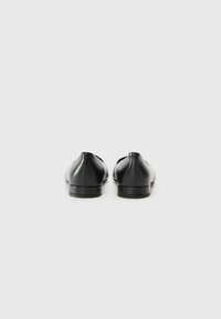 Chaussures en cuir noir avec un design discret, texture lisse, bout rond et talon plat, montrant une vue arrière minimaliste.