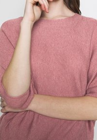 Rosenfarbener Strickpullover mit Rippstruktur, kurzen Ärmeln und lockerer Passform, mit einem runden Ausschnitt und dezenten Falten.