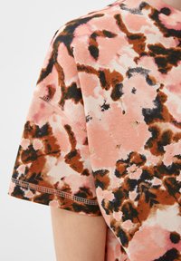 Korte mouwen, blush roze stoffen t-shirt met een bloemenprint in bruin- en zwarttinten; heeft gestikte randen en een zachte textuur.