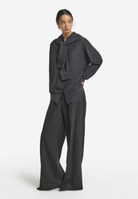 Mörkrandig långärmad blus med en stor krage och knytdetalj, i kombination med vida mörka byxor gjorda av ett slätt tyg.