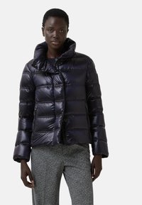 Krótka kurtka puchowa w błyszczącym, ciemnoniebieskim kolorze. Posiada pikowaną teksturę, wysoki kołnierz, zatrzaski oraz kieszenie boczne na zamek błyskawiczny.