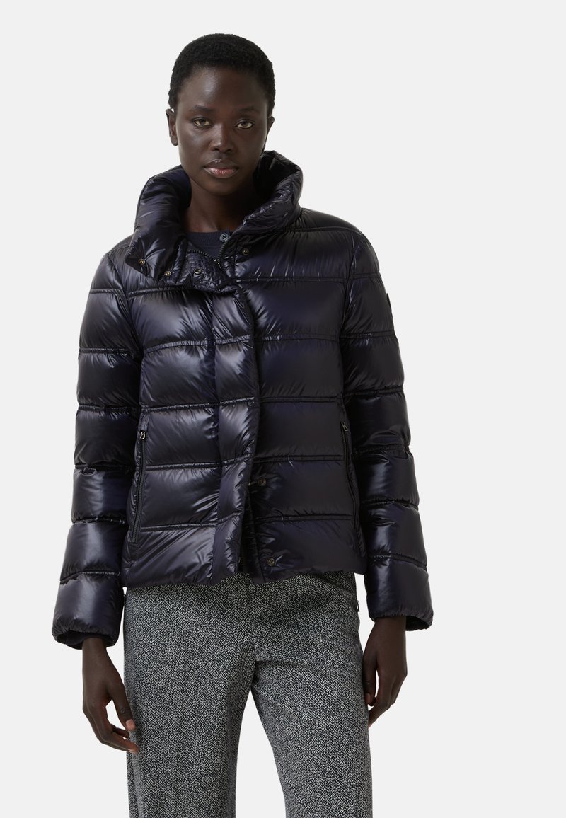 Krótka kurtka puchowa w błyszczącym, ciemnoniebieskim kolorze. Posiada pikowaną teksturę, wysoki kołnierz, zatrzaski oraz kieszenie boczne na zamek błyskawiczny.