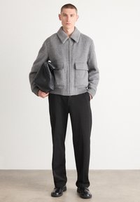 Gray herringbone jacket with a collared neckline, two front pockets, and a zip closure, paired with black trousers and shoes.