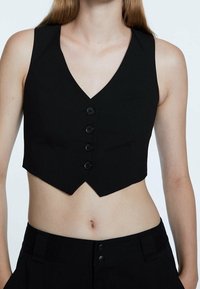 Canottiera nera corta con scollatura a V, caratterizzata da cinque bottoni, un design aderente e una texture del tessuto liscia, accentuata da bordi netti.