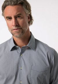 Košilové triko v černo-bílém geometrickém vzoru; má knoflíky, decentní detail kapsy a volný střih.