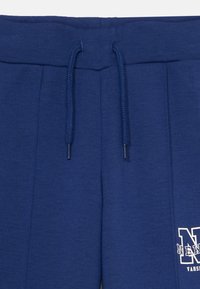 Námornícke modré teplákové nohavice s nastaviteľným pásom, jemnou textúrou, záhybmi vpredu a bielym potlačeným logom.