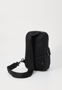 Sort skuldertaske med en struktureret mesh-bagside, justerbar rem, lynlåslukning og afrundet form. Har flere rum og slidstærkt materiale.