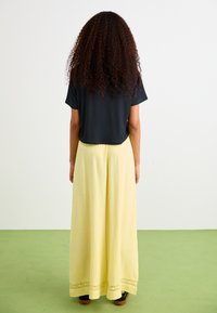 Black short-sleeve top paired with a long, textured yellow skirt featuring a lace trim along the hem. Worn with black footwear.