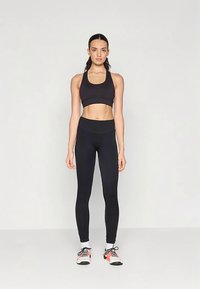 Black sports bra and high-waisted leggings, both made of stretchy material. Model stands against a light background, wearing athletic shoes.
