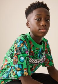 Groen T-shirt met korte mouwen met Minecraft-thema, met diverse kleurrijke afbeeldingen van personages, blokken en diamanten.