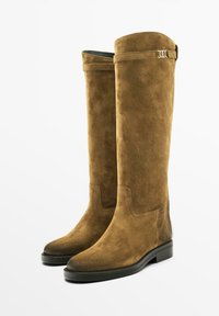 Stivali al ginocchio in camoscio marrone con punta tonda, suola piatta in gomma e una fascia decorativa con fibbia dorata nella parte superiore.